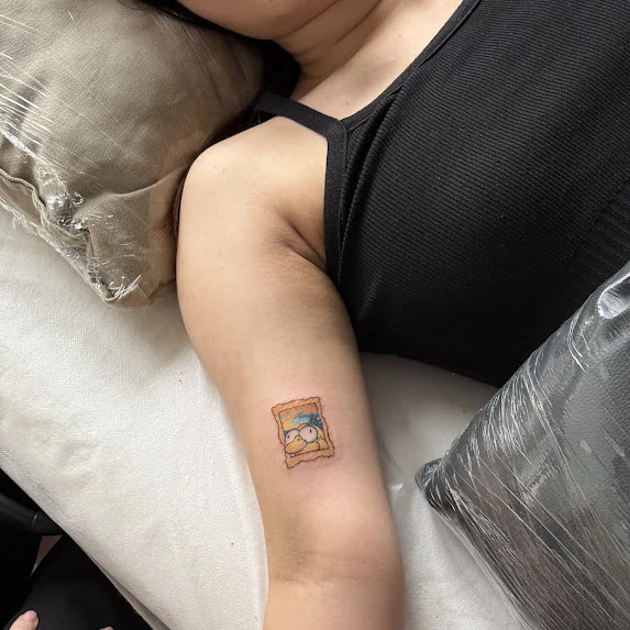 The stamp sized framed painting tattoo on an upper arm