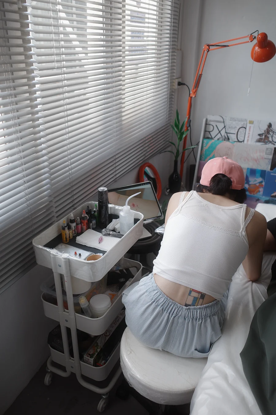 ピンクのキャップのアーティストが腕に向かって前かがみになり、ワゴンのiPadに桜のデザインが映っている
