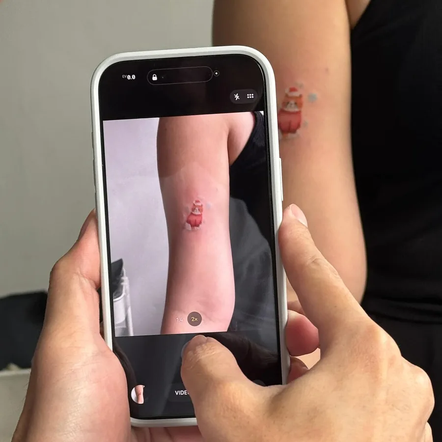 A phone photographing the freshly finished Christmas cat tattoo on an upper arm