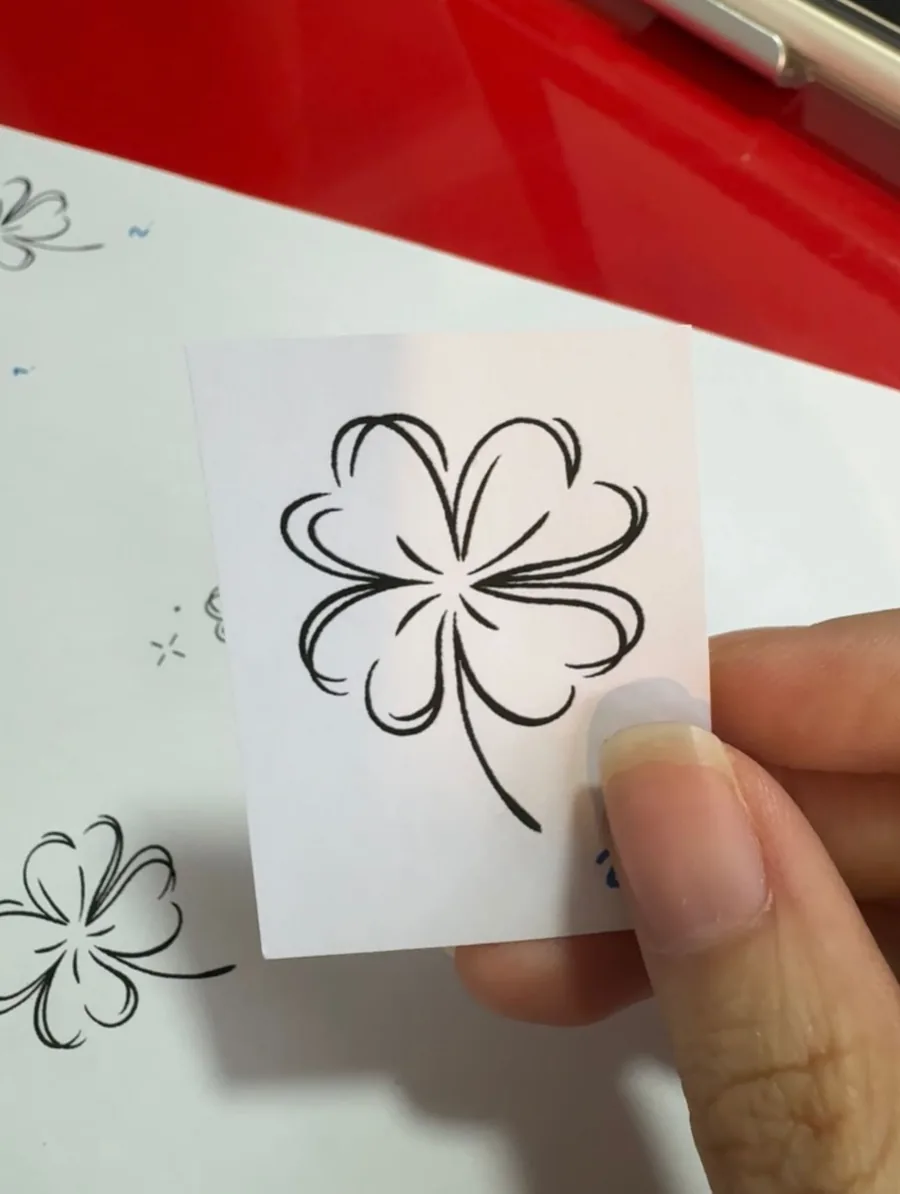 A hand holding the clover design card, with a sheet of numbered colour options behind