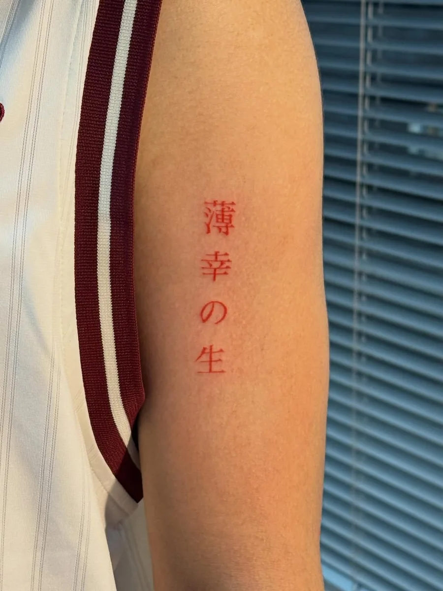 Vertical Japanese lettering tattooed entirely in red ink on an upper arm
