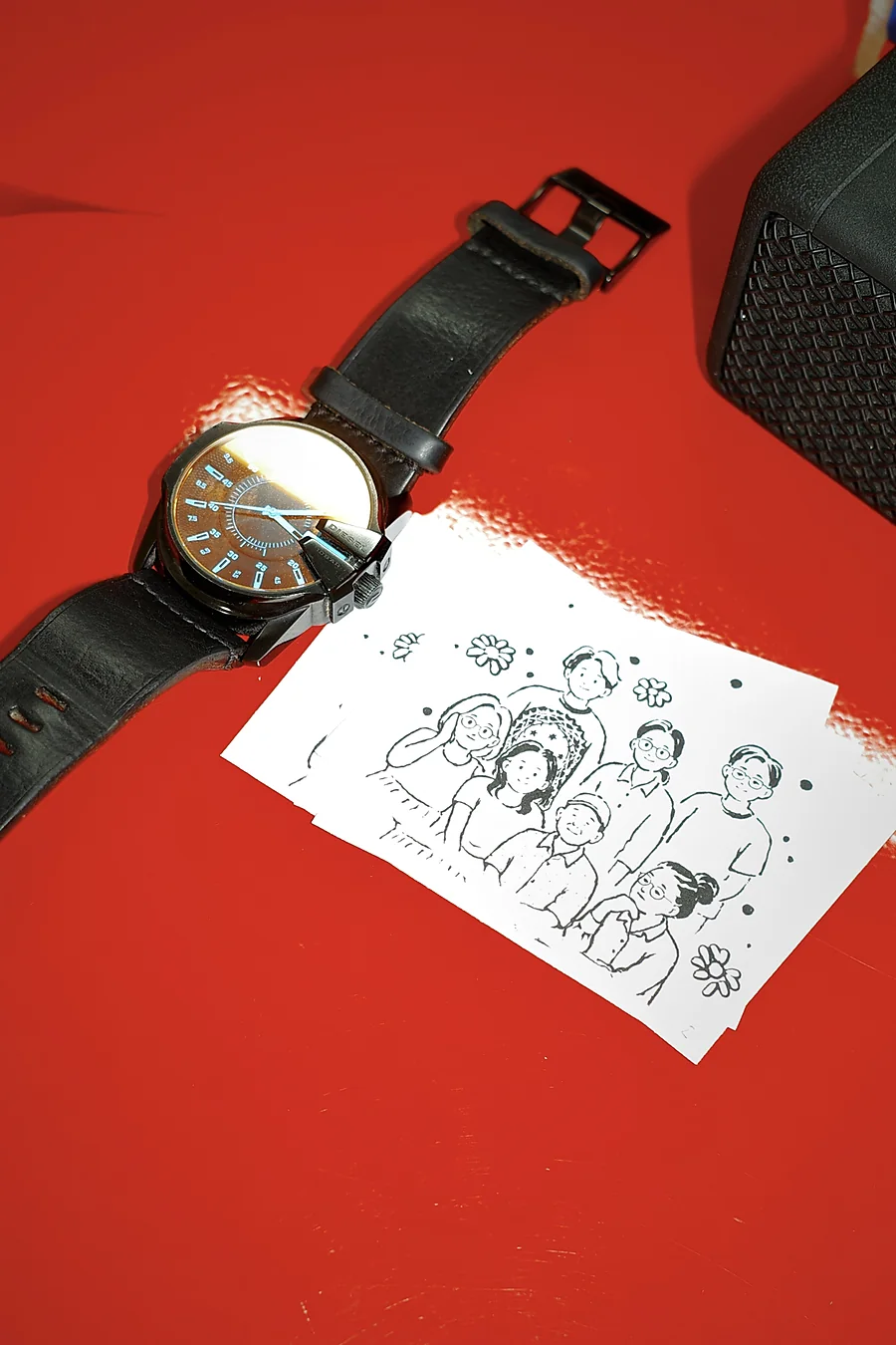 The printed family portrait design on a red table next to a wristwatch before the session