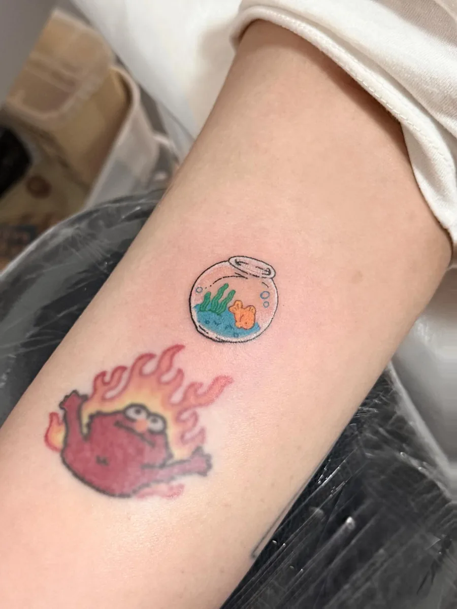 The goldfish bowl tattoo on a forearm, sitting above the client's older tattoo