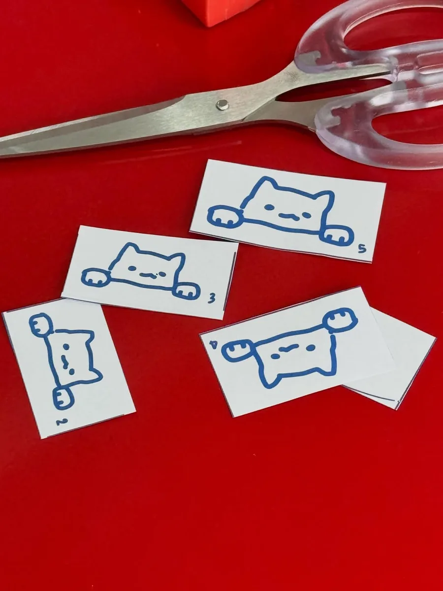 Five numbered paper cutouts of the cat character in different poses, on a red table with scissors