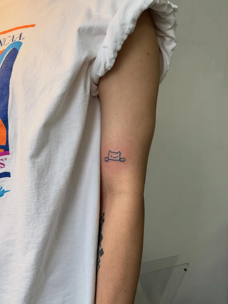 Placement of the blue cat tattoo on the back of the upper arm, visible in a t-shirt