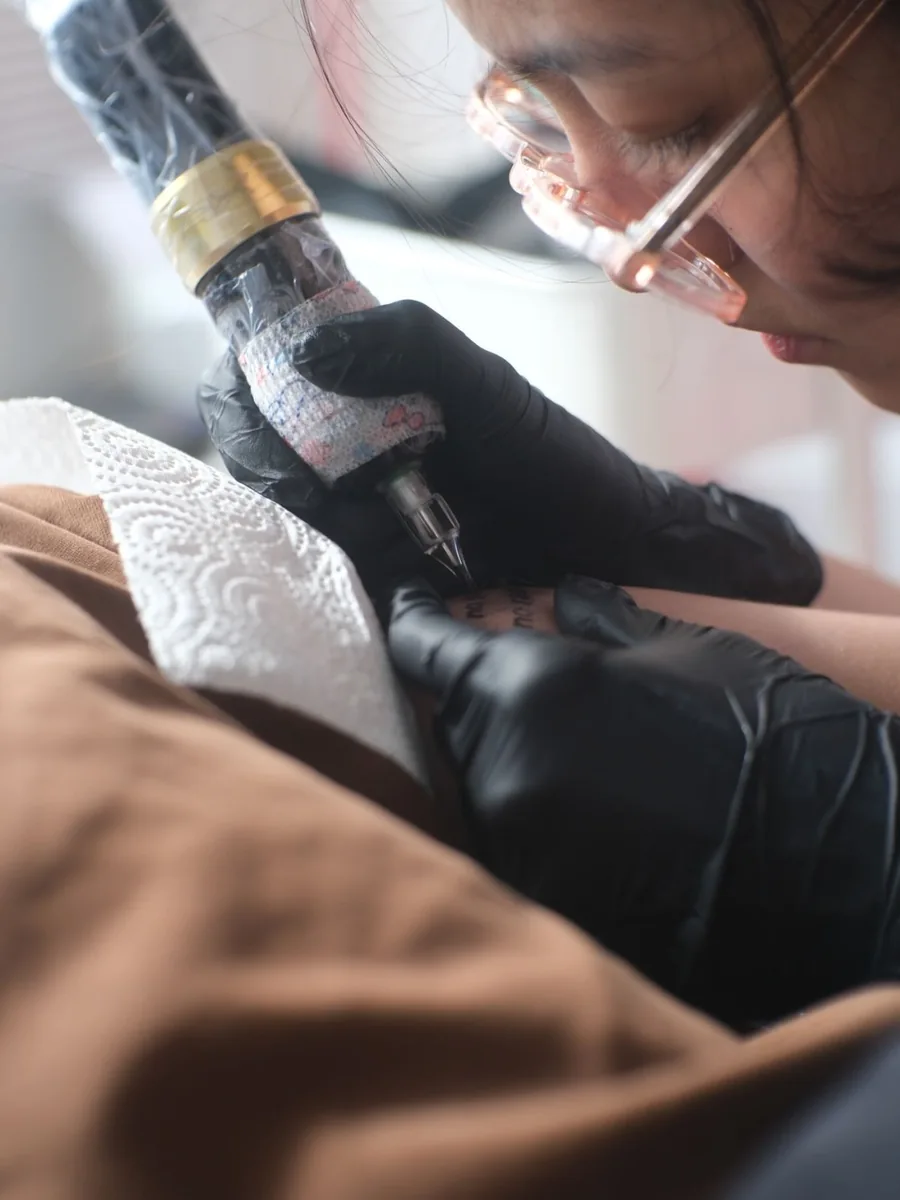 The artist carefully tattooing the lettering on the client's arm