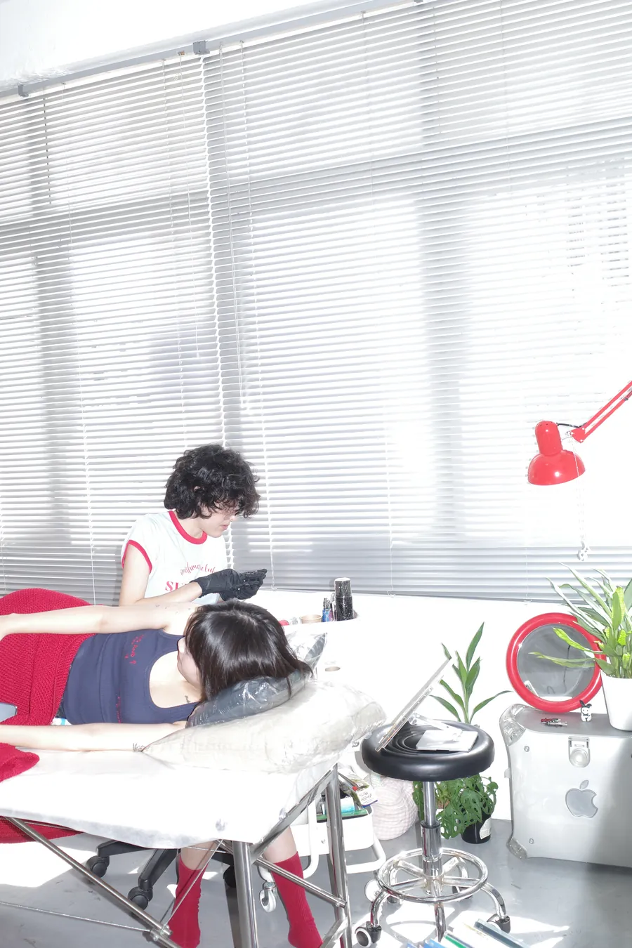 白いブラインド、赤いデスクライト、植物のある明るい施術室