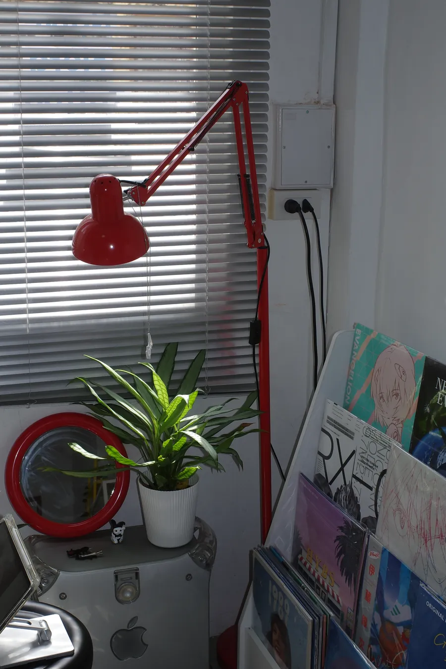 赤いデスクライト、赤いふちの丸い鏡、植物、レコード棚があるスタジオの一角